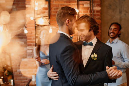 Dreamy portrait of young gay couple dancing together during wedding reception with lens flareの写真素材