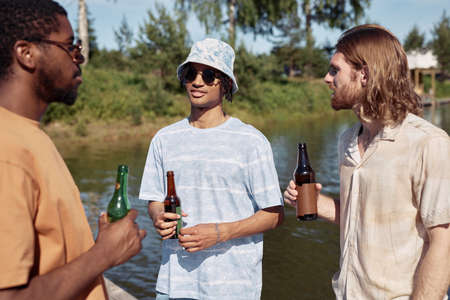 Waist up portrait of three young men drinking beer outdoors and chatting in Summer setting