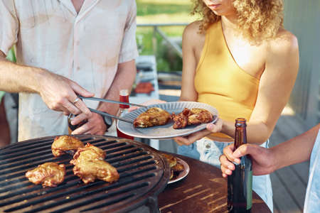 Close up of friends grilling chicken meat during barbeque party outdoors in Summerの写真素材