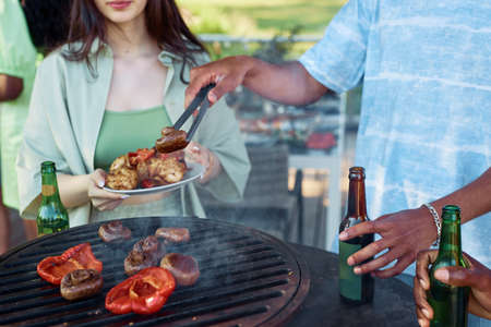Close up of friends grilling vegetables while enjoying vegetarian barbeque party outdoors in Summerの写真素材