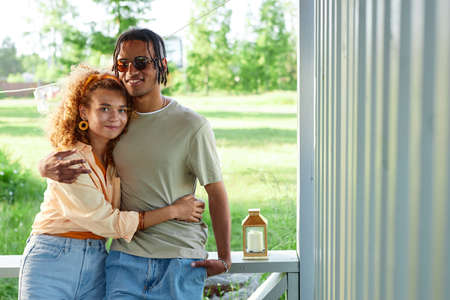 Waist up portrait of loving black couple embracing and looking at camera at outdoor terrace in Summer, copy spaceの写真素材