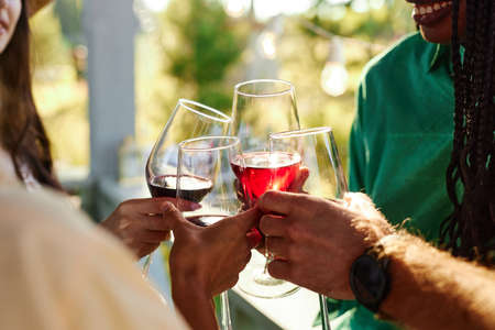 Close up of friends toasting with wine glasses in celebration during outdoor party in Summerの写真素材