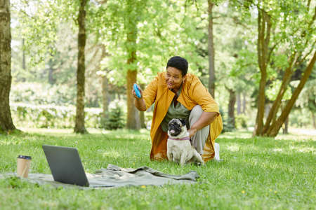 Full length portrait of cute mature woman playing with dog in park and throwing toys in green grass,...