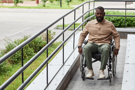 Full length portrait of adult black man with disability going down ramp in city, urban accessibility