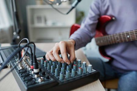 Close up of young woman turning controls on switchboard panel while recording music at home, copy...