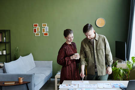 Young man pointing at documents with charts on table and discussing it with woman during their work at homeの写真素材