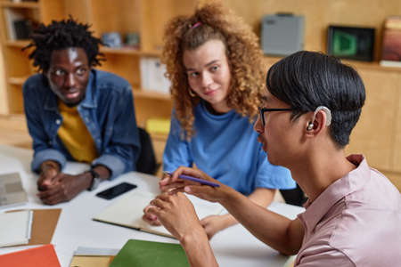 High angle portrait of young Asian man speaking to group of students in library, copy spaceの写真素材