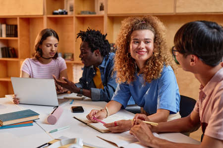 Diverse group of students working at table in library together, focus on smiling young woman with curly hairの写真素材