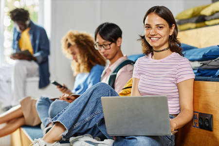 Diverse group of students in row studying, focus on smiling young woman using laptop in foreground,...
