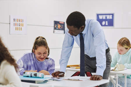Portrait of young male teacher helping smiling girl studying in school classroom, copy spaceの写真素材