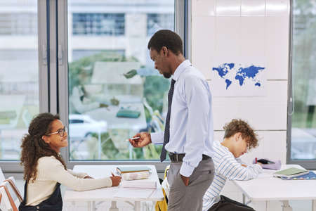 Side view portrait of young black teacher working with kids in school classroom