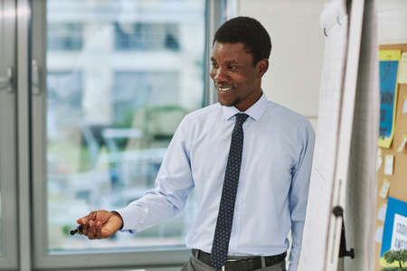Side view portrait of smiling black teacher standing by whiteboard and talking to class