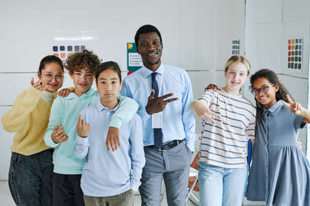 Portrait of smiling teacher posing with diverse group of children and showing hand signsの写真素材