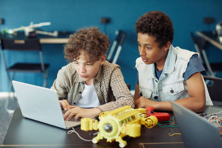 Portrait of two teenage boys using laptop and programming robot during engineering class in schoolの写真素材