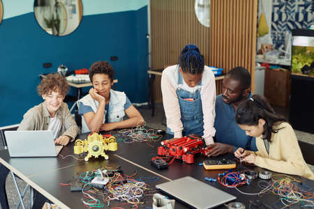 Diverse group of kids with male teacher building robots together during engineering class in schoolの写真素材