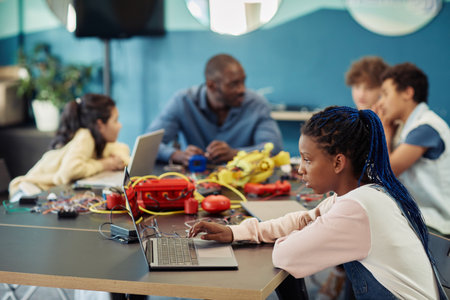 Side view portrait of young black girl using laptop in engineering class and programming robots, copy spaceの写真素材