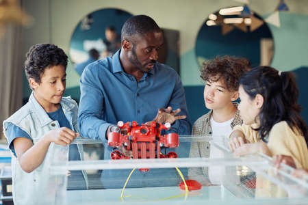 Portrait of black male teacher demonstrating robotic boat to diverse group of children in engineering classの写真素材