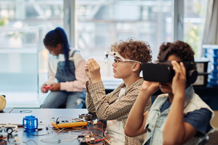 Side view portrait of two kids building robots in engineering class and using VR technologyの写真素材