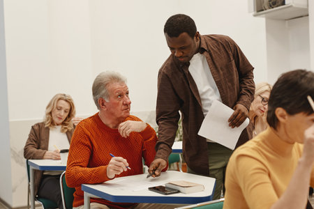 African young teacher walking along the class and explaining adult students how to write testの写真素材