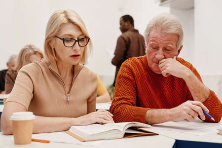 Senior couple sitting at desk and reading a book together during training in classの写真素材