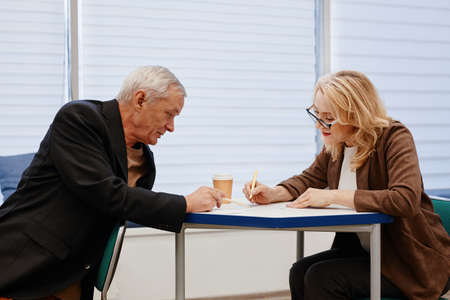 Senior man asking question to woman while she explaining him new topic during training