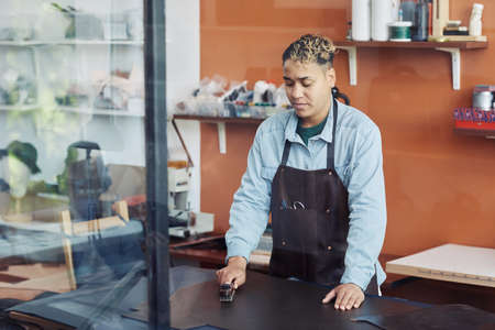 Waist up portrait of young artisan prepping leather in studio and creating handmade pieces, copy...