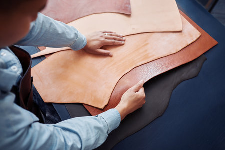 Close up of craftsman working with genuine leather pieces on table in tannery shop, copy space