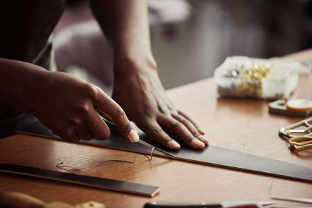 Close up of black young woman cutting leather and creating handmade belt in workshop, copy spaceの写真素材