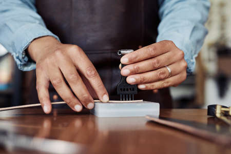 Close up of anonymous modern artisan punching holes in handmade leather belt at workshop, copy spaceの写真素材