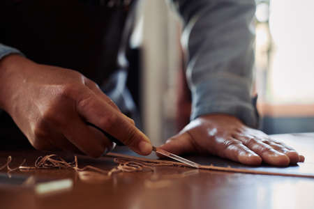 Close up unrecognizable artisan shaving leather piece in workshop, copy spaceの写真素材