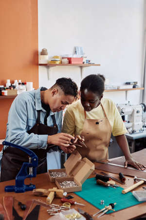 Vertical portrait of two female artisans in leatherworking shop creating handmade pieces together