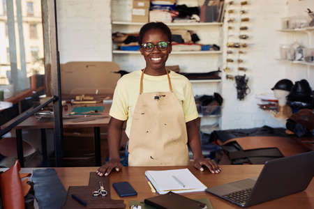 Portrait of female small business owner smiling at camera while posing in leatherworking workshop, copy spaceの写真素材