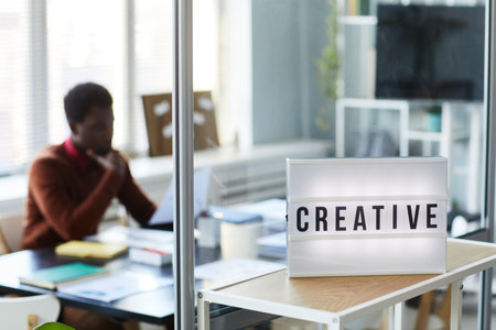 Background image of CREATIVE light up sign on table in office with person working, copy spaceの写真素材