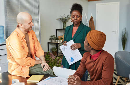 Portrait of successful black businesswoman talking to two colleagues in office while managing projectの写真素材