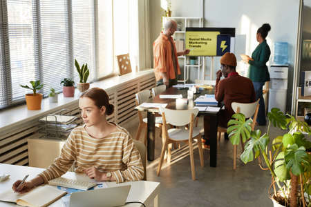 Wide angle view at creative young people working in office with focus on woman at workplace, copy spaceの写真素材