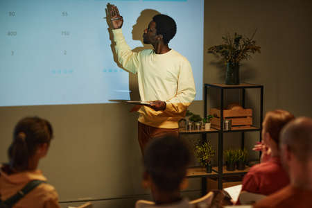 Minimal side view portrait of young black man giving presentation by projector screen during business meeting or training session, copy spaceの写真素材