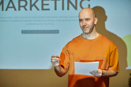 Waist up portrait of marketing expert giving presentation by projector screen and addressing audience in business training, copy spaceの写真素材