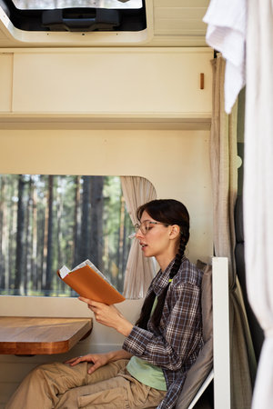 Young girl in eyeglasses reading a book sitting in house of wheels during tripの写真素材