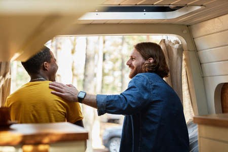 Rear view of friends talking to each other while sitting in motorhome during camping in the forest