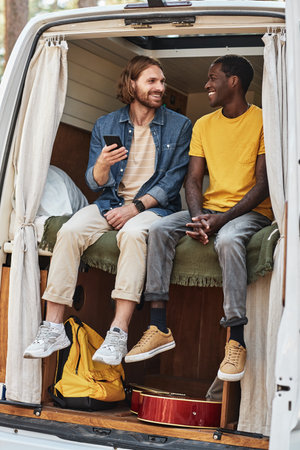 Two friends resting in van during camping, they using mobile phone and talking