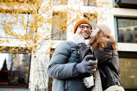 Young woman kissing her boyfriend during their walk in the city in autumn dayの写真素材