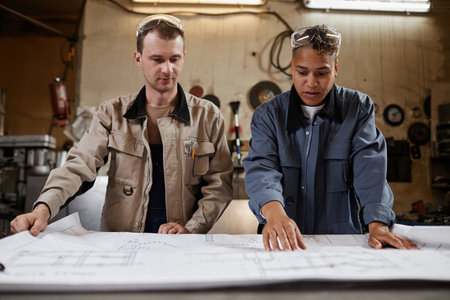 Front view portrait of two workers inspecting blueprints and plans in industrial factory workshopの写真素材