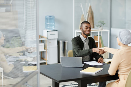Wide angle of young black man shaking hands with female HR manager after successful job interview in office setting, copy spaceの写真素材
