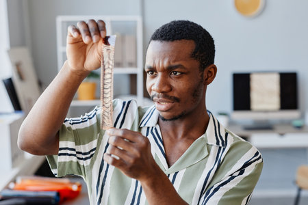 Portrait of black male photographer looking at film against light and making selection while working in photo studioの写真素材