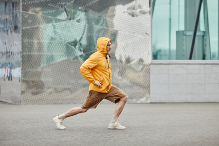 Minimal side view portrait of sportive mature man stretching outdoors in urban city setting and wearing contrasted yellow jacketの写真素材