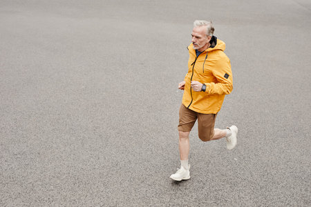 Minimal high angle portrait of handsome mature man running outdoors against concrete background and wearing contrasted yellow jacket, copy spaceの写真素材