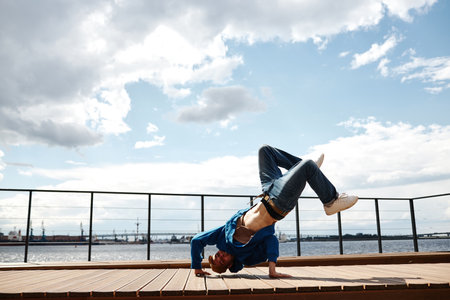 Full length shot of male hip-hop dancer posing outdoors and doing handstand against sky, copy spaceの写真素材
