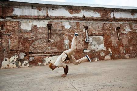 Wide angle shot of young man doing breakdance handstands outdoors in shabby urban setting, copy spaceの写真素材