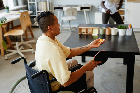 High angle portrait of young woman with disability playing table tennis in office, inclusivity at workplace conceptの写真素材