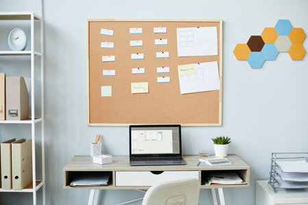 Background image of open laptop at workplace with corkboard in minimal office interior, task management setup, copy spaceの写真素材